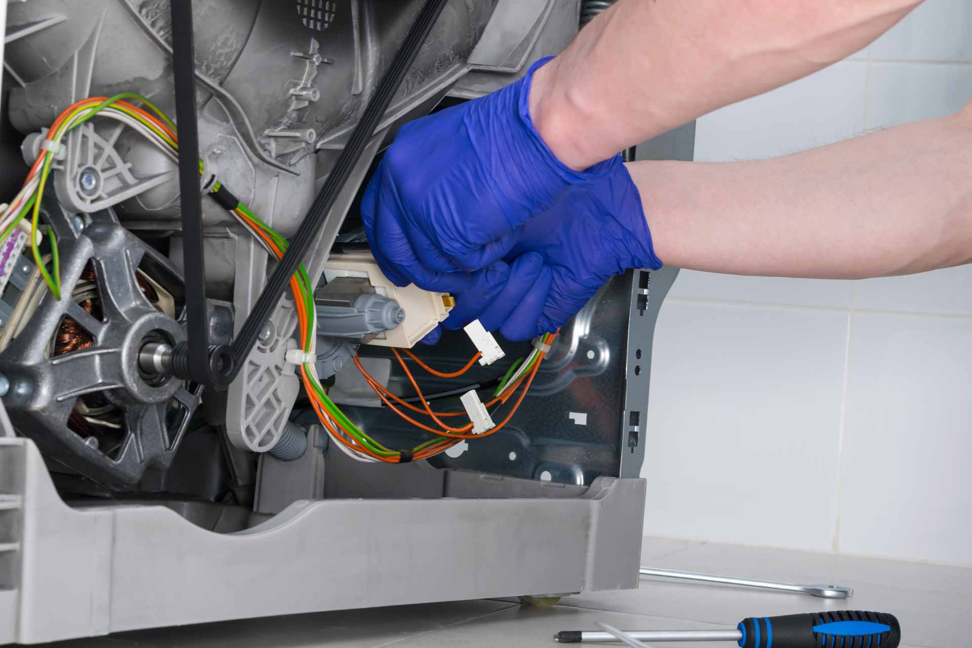 Close up on appliance repair technician's hands removing a faulty part from a washer/dryer