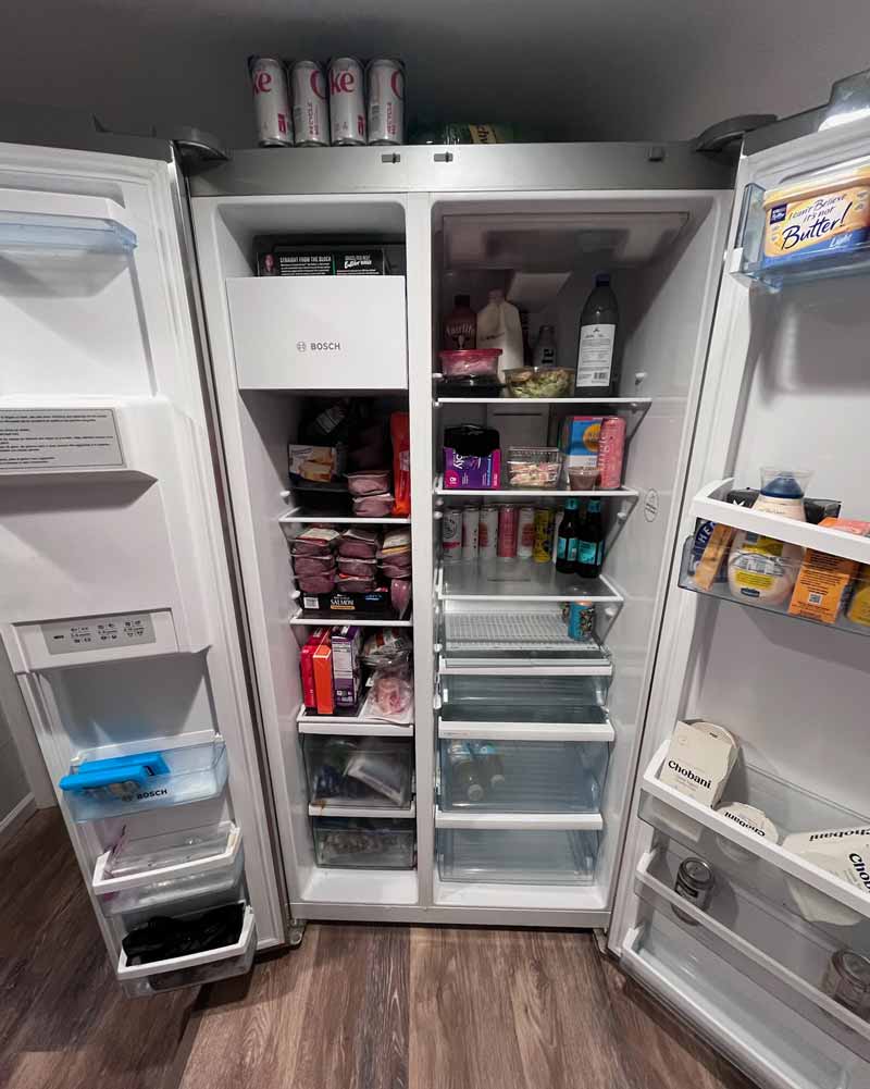 A Bosch refrigerator. The doors are open and it's full of food, but the lights aren't on